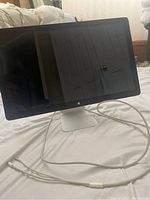 Front angled view of the 28 inch Apple monitor on white bedspread showing screen, Apple logo, and attached Lightning cable in natural indoor lighting.