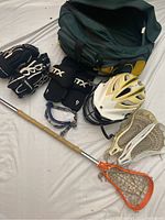 Full set of used women's lacrosse equipment displayed with bag, helmet, gloves, pads, stick with head, and goggles shown.