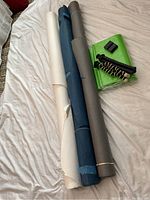 Three rolls of background paper in white, blue, and gray colors, laid out on a bed with two flexible tripods and a folded green canvas background visible.