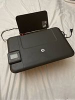 Photo of HP DeskJet 3052A printer showing overall device with rear paper input tray and power cord connected.