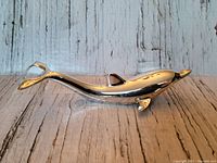 Side view of a shiny metal dolphin bottle opener on a wood-textured surface.