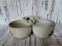 Photo showing the side view of the speckled cream pottery trio with loop handle and flower petal decoration on one bowl.