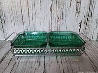 View of two square emerald green glass dishes placed side by side within a silver-tone decorative metal serving tray with handles.