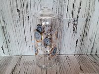 Front view of vintage clear glass canister decorated with pale blue and gold floral patterns placed against a rustic wooden background