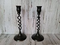 Pair of black twisted metal candlesticks shown front facing on white rustic wood background.
