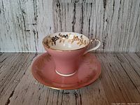 Pink vintage Aynsley teacup and saucer set with gold floral detailing and gold trim in excellent condition.