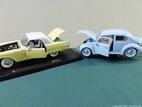 Photo showing Ford Thunderbird (yellow with white roof) and Volkswagen Beetle (baby blue) model cars side by side with open doors and hoods.