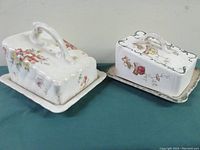 Pair of antique cheese or butter dishes with lids, each on a tray, showing floral designs and crazed glaze