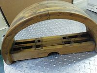 Full view of the curved wooden half mill wheel piece sitting on a metal surface, showing the external shape and top slots