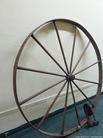 Full view of large wooden great/walking wheel with multiple spokes attached to hub and floor base.