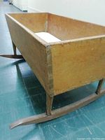 Side view of the wooden cradle showing the rectangular body and curved rocker base on a green floor.