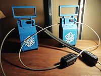 Pair of blue USA Covell Ski Tote locks with attached flexible steel cables, displayed upright in a room with wooden surface and dark background.