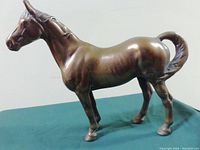 Side view of brass horse figurine showing polished surface and detailing on head, legs, and tail.
