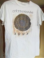 Front of Whitesnake 1987 tour T-shirt showing band logo, tour emblem, and year printed in black and gold colors on white background.
