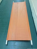 Orange fabric stretcher with metal frame laid flat showing full length and fabric detail.