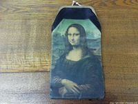 Front view of cloth case showing Mona Lisa printed image, metal kiss-lock frame visible, placed on wooden surface