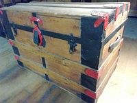 Front and side view of the large wooden steamer trunk showing red-painted metal corner protectors and black metal lock with red latch.