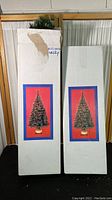 Two tall cardboard boxes, each containing one fiber optic Christmas tree, packaging shows images of the tree lit up.