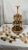 Full view of assembled three-tier wooden Christmas pyramid with detached pieces including figurines and fan blades separated in front.