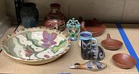 Overview of the Latin themed pottery collection showing various ceramic and terra cotta pieces including a large painted bowl, animal figures, a decorative tree figurine, several small dishes and vases.