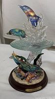 Full view of the limited edition figurine showing dolphins jumping out of translucent water splash on wooden base