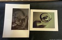 Two original prints by Randolph Johnson shown side by side on a dark surface. One depicts a stylized face in water, the other a glass of water.