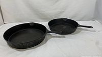 Two cast iron skillets side by side on white background showing size difference and wear