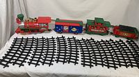 Photo showing the entire train set with four train cars lined up behind twelve curved black track pieces on a white surface.