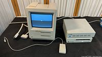 Full shot showing Macintosh SE computer and two external drives on table with cables and mouse wired to computer.