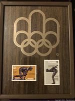 Wooden box lid with gold Olympic rings and two individual Canada stamps ($1 and $2) showing Olympic athletes diving and skating.