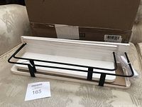 Shelf showing flat whitewash finished wood base with black metal railing on top and mounting hardware attached underneath.