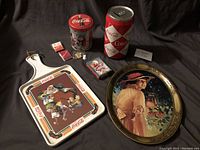Full overview of Coca-Cola collectibles including metal tray, large coin bank tin can, smaller tin can, and other small collectible items.