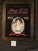 Full view of vintage Coca-Cola wall art featuring an elegant woman and classic Coca-Cola logo in wood frame.