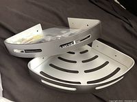 Two images showing the corner shower shelf, focusing on the full shelf shape and mounting bracket area, highlighting the polished silver/chrome metal finish and vented design.