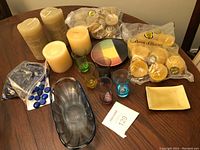 Full lot on table showing large candles, small packaged beeswax tarts, multiple glass holders, decorative stones, colorful decor disc, and ceramic tray.