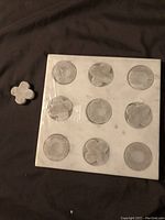 Marble tic tac toe game board with nine marked spaces and one piece beside it showing circular and cross shapes.