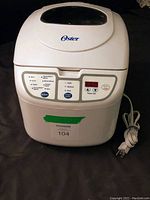Full front view of Oster bread maker showing overall appliance with lid, power cord, and control panel.