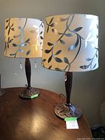 Pair of decorative table lamps on wooden table, showing bases and leaf patterned fabric drum lampshades.