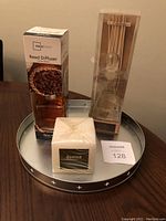 Full view of reed diffuser, candle, and metal tray on wooden table.