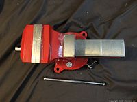 Side view of red painted cast iron bench vise with swivel base and removable chrome steel handle.
