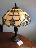 Full view of Tiffany style table lamp with stained glass shade and metal base on wooden table.