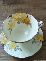Top-down view of Aynsley bone china tea cup and saucer with yellow rose design and gold trim, showing floral pattern inside cup and on saucer.