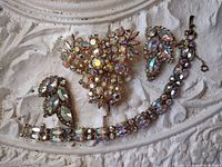 Three-piece rhinestone set including bracelet, pair of earrings, and brooch arranged on decorative white background.