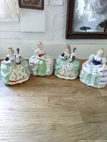 Front view of four lady dresser jars arranged in a row, highlighting different dresses and instrumental details.