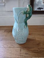 Front view of light blue ceramic vase with butterfly design and green frog climbing the side.
