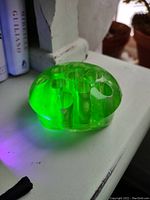 Side view of green uranium glass flower frog glowing under UV light showing translucent nature and multiple holes.