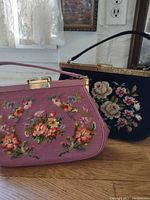 Two vintage needlepoint handbags displayed side-by-side on a wooden surface, showing the front floral needlepoint designs and handle attachments.
