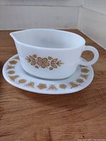 Front and side view of the white Pyrex gravy boat and matching saucer showing brown floral decoration