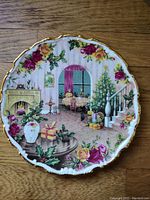 Front photo of the Royal Albert Christmas Magic plate showing colorful Christmas indoor scene with decorated tree, gifts, fireplace, and floral border with gold trim.