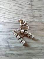 Pair of signed Sherman screw-on earrings lying on a wooden surface. Linear drop design with clear rhinestones and screw backings.